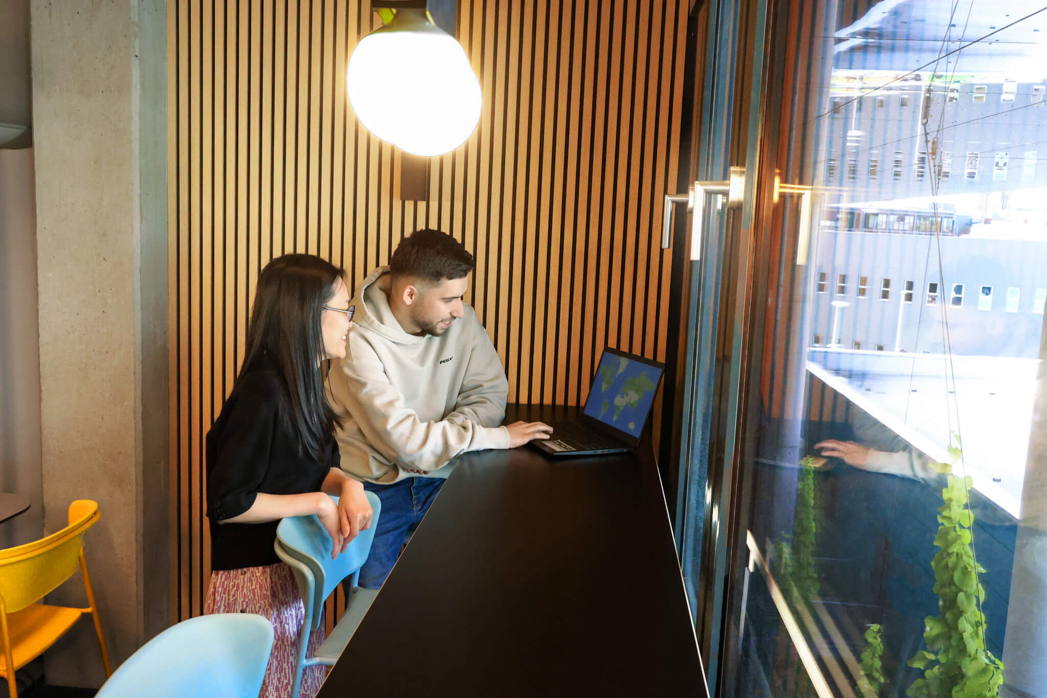 Zwei Mitarbeiter der 1000hands AG arbeiten an einem Laptop vor einer großen Fensterfläche.